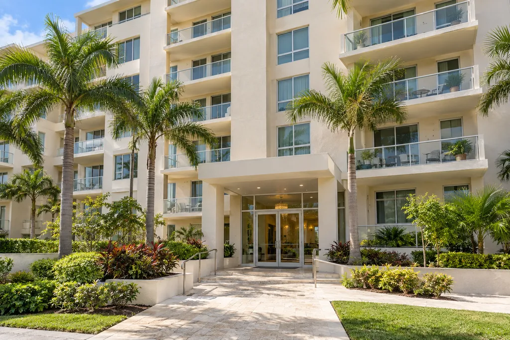 A modern building with balconies and palm trees in front.